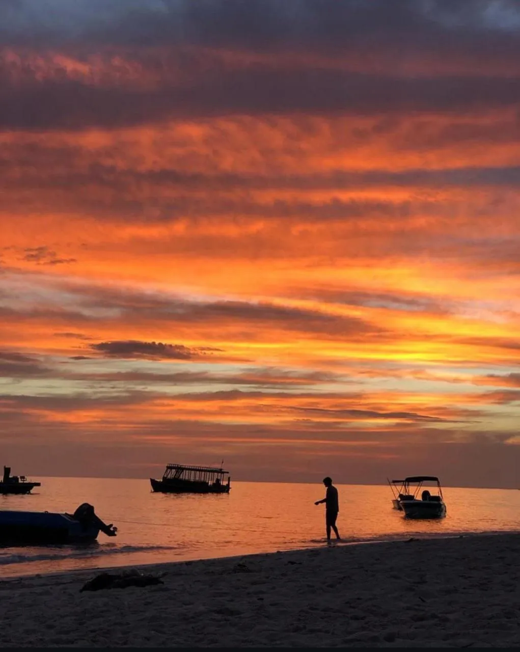 Coucher de soleil sur la mer avec des bateaux et une personne sur la plage.