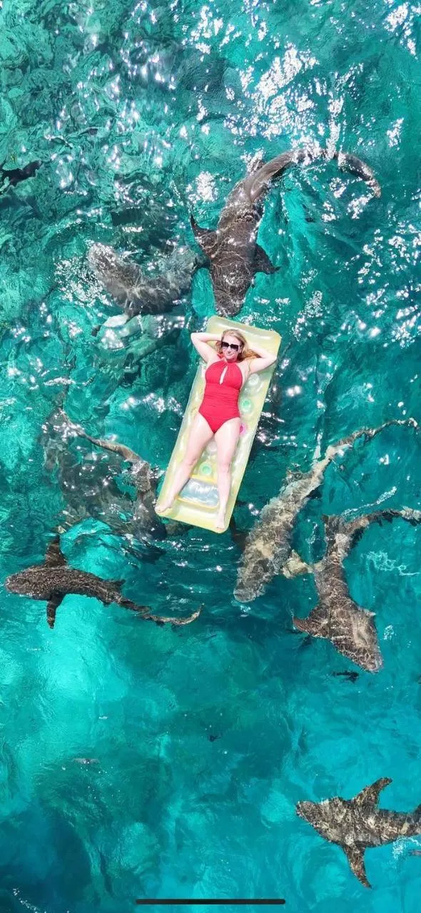 Une femme se détend sur un matelas flottant dans une eau turquoise entourée de raies.
