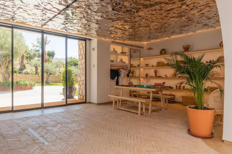 Espace lumineux avec une table en bois et des étagères décoratives, ouvert sur un jardin verdoyant.