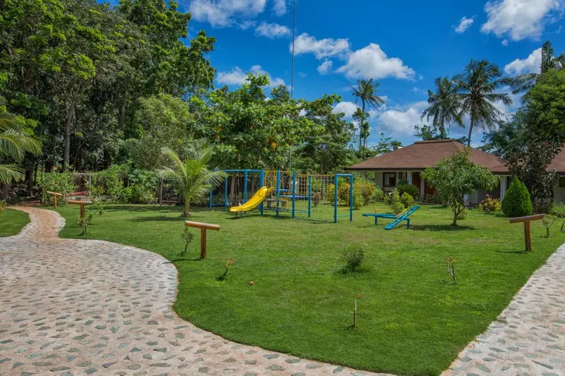 Une aire de jeux colorée se trouve sur une pelouse verdoyante dans un jardin tropical.