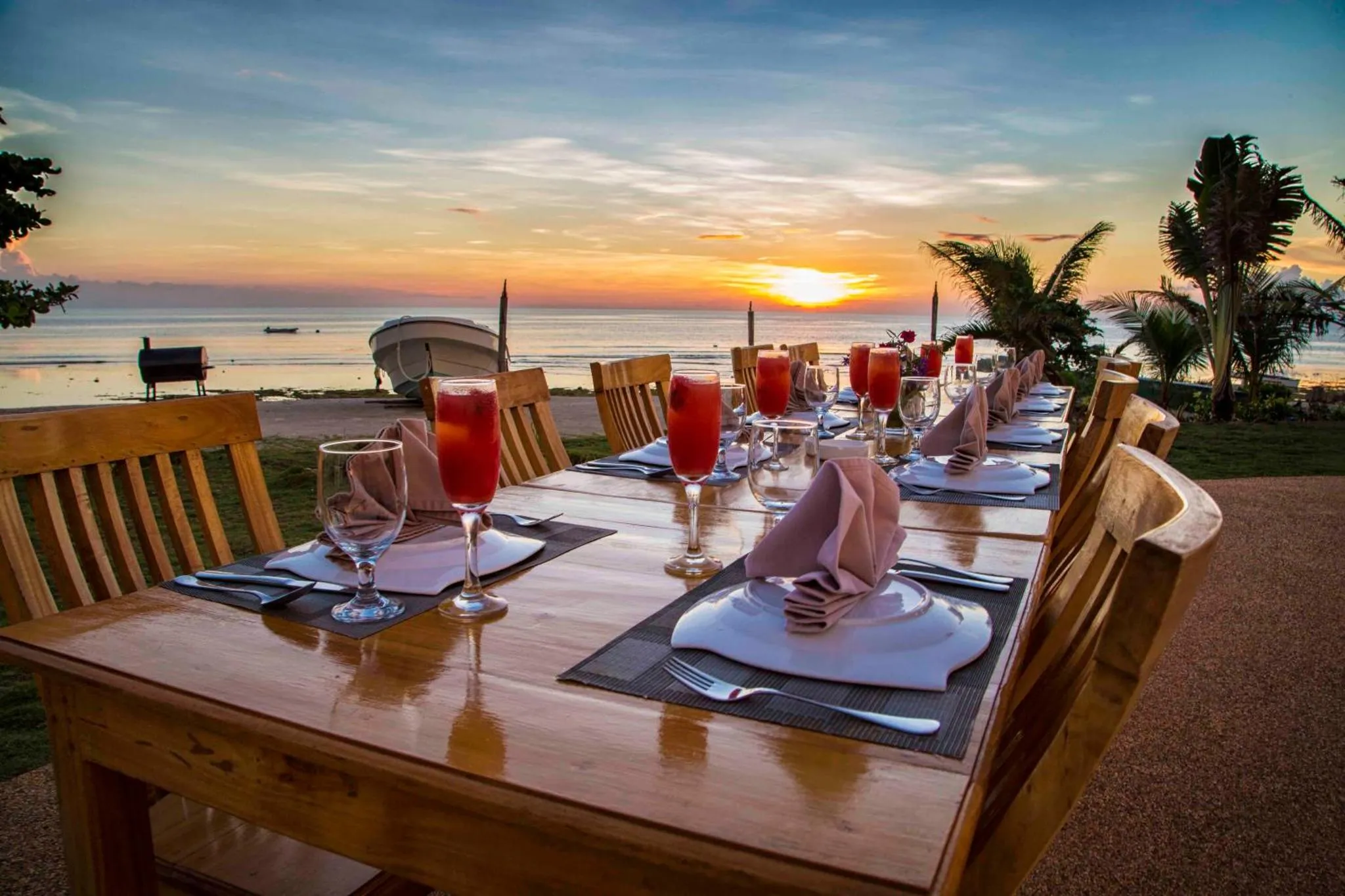 Une longue table est dressée pour un dîner en extérieur face à la mer au coucher du soleil.