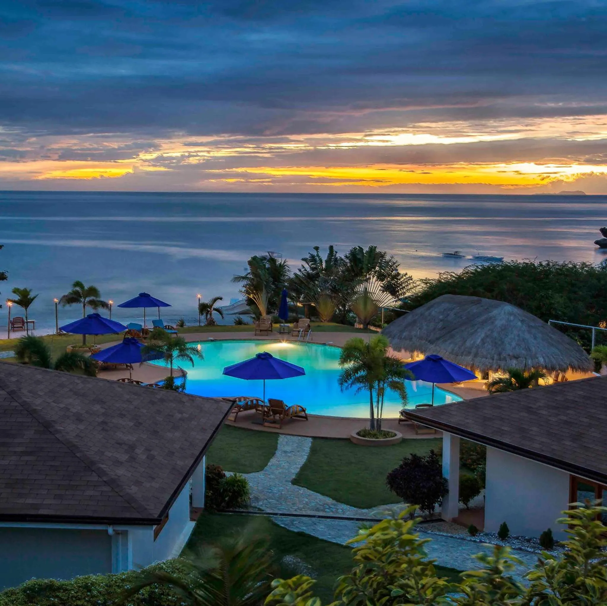 Vue d'une piscine illuminée au crépuscule avec des transats et des parasols.