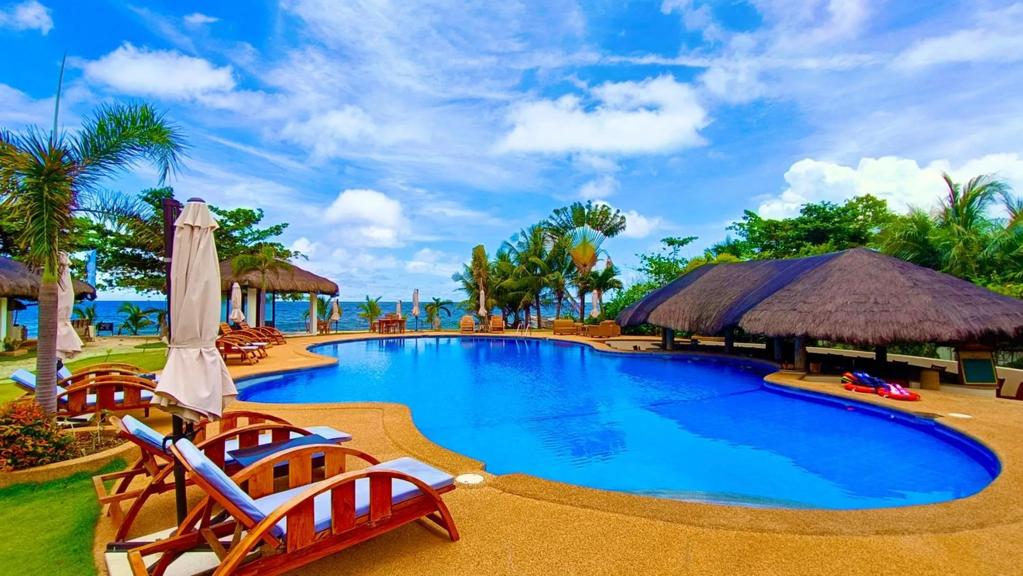 Une piscine bleue bordée de chaises longues sous des parasols, avec une vue sur la mer.