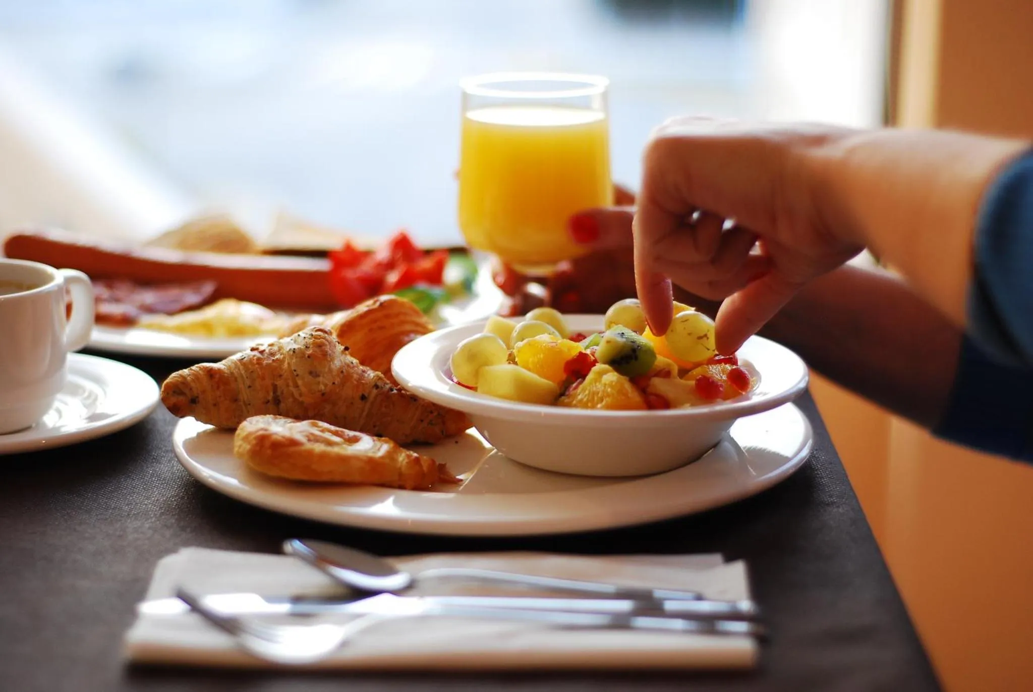 Une table est dressée avec un petit-déjeuner composé de fruits, viennoiseries et boissons.