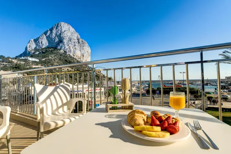 Une table est dressée sur une terrasse avec un petit-déjeuner et une vue sur la mer et un rocher.