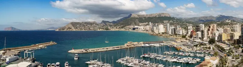 Vue panoramique d'une ville côtière avec un port de plaisance et des montagnes en arrière-plan.