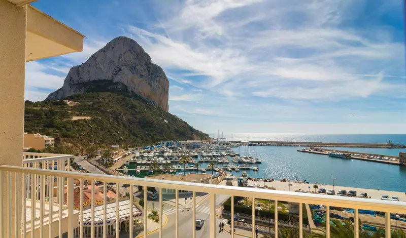Vue d'un port de plaisance et d'une montagne rocheuse depuis un balcon.