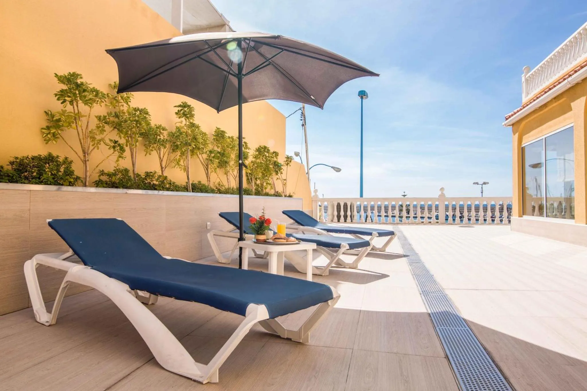 Transats bleus sur une terrasse ensoleillée avec vue sur la mer.