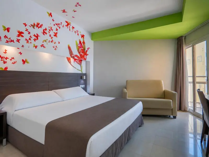 Une chambre lumineuse avec un grand lit et un canape beige.