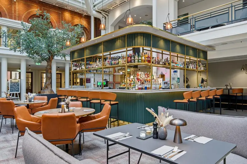 Un bar spacieux avec des tabourets et des tables à manger dans un hall lumineux.