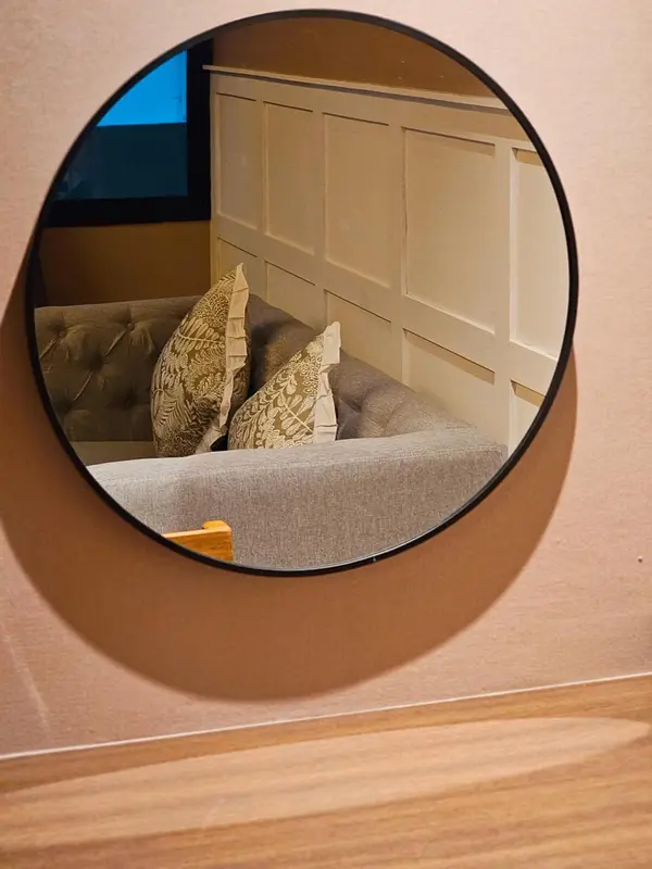 Un lit avec des oreillers est visible dans le reflet d'un miroir rond.