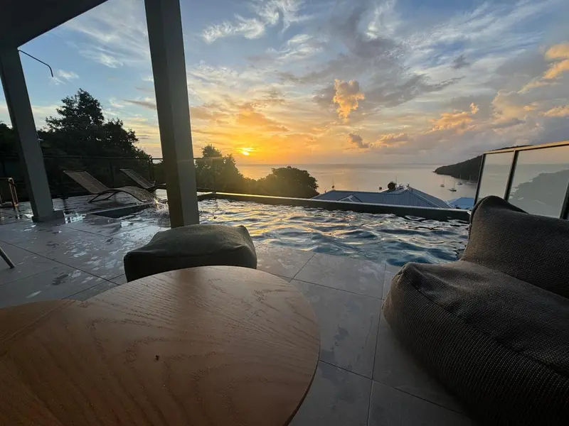 Terrasse avec piscine à débordement et vue sur la mer au coucher du soleil.