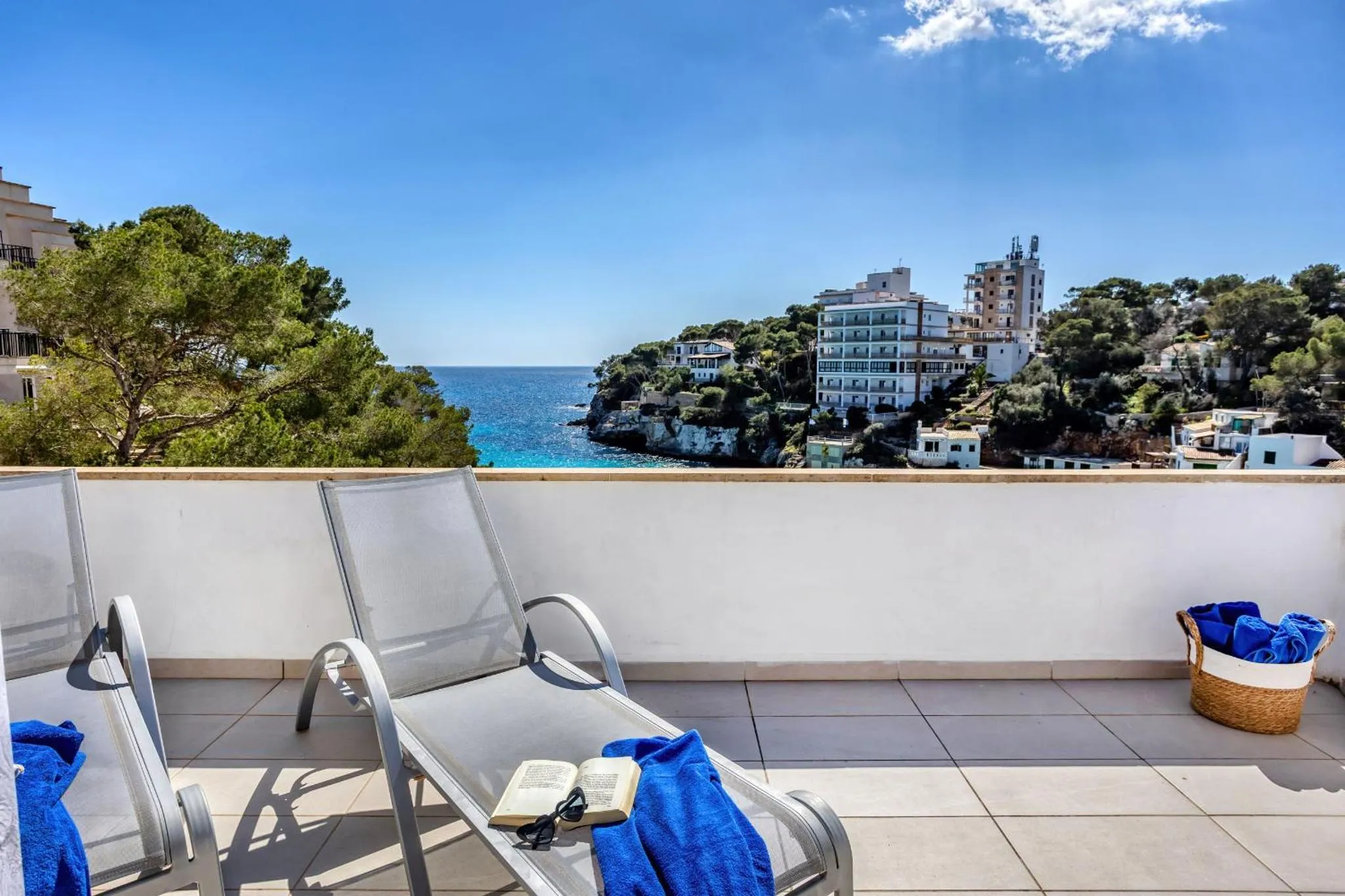 Deux transats bleus sur une terrasse ensoleillée avec vue sur la mer.