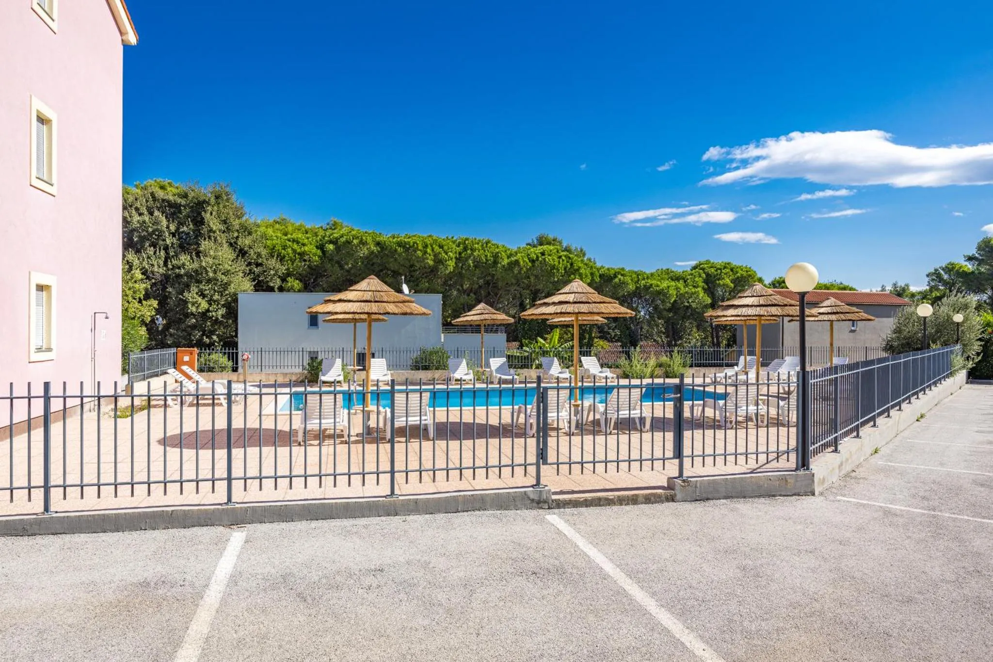 Transats et parasols ombragent une piscine rectangulaire entourée d'une terrasse.