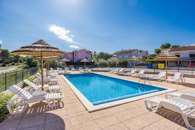 Transats blancs disposés autour d'une piscine rectangulaire ensoleillée.