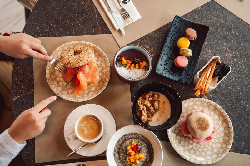 Une table est dressée avec un petit-déjeuner composé de viennoiseries, de fruits et de boissons.