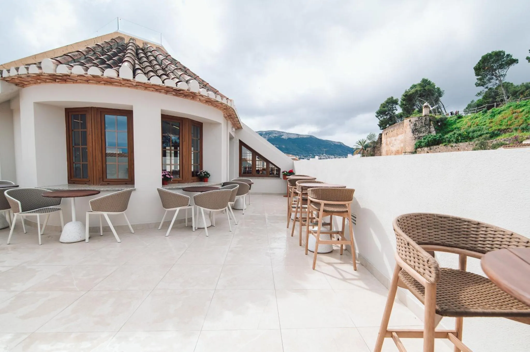Terrasse avec tables et chaises offrant une vue sur la mer et les montagnes.