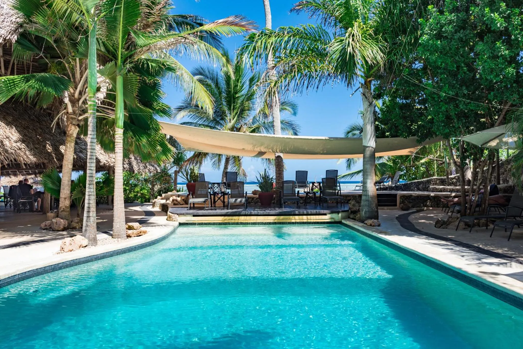 Une piscine turquoise bordée d'une terrasse ensoleillée avec des transats.