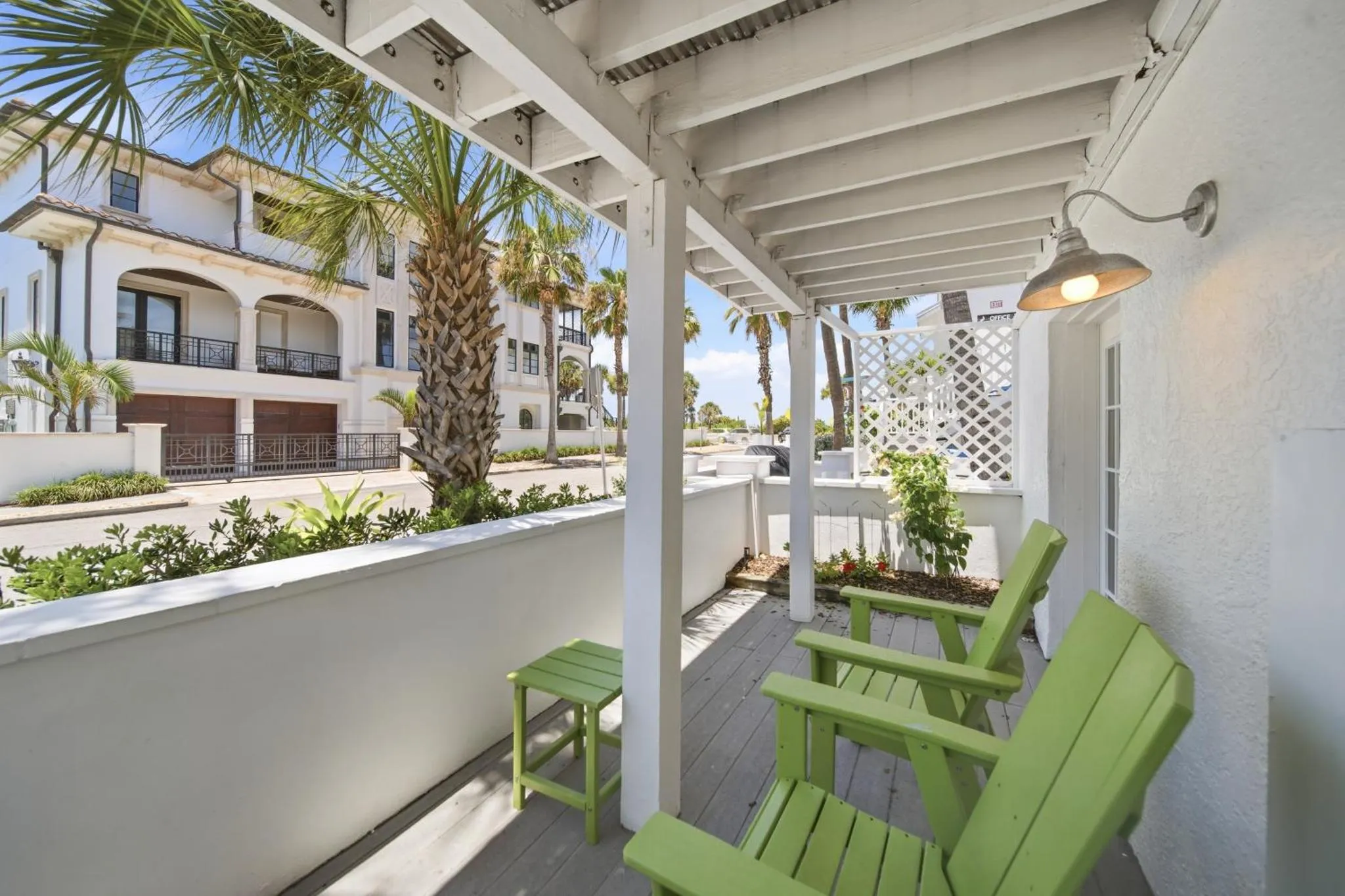 Terrasse ombragée avec mobilier en bois vert et vue sur un bâtiment.