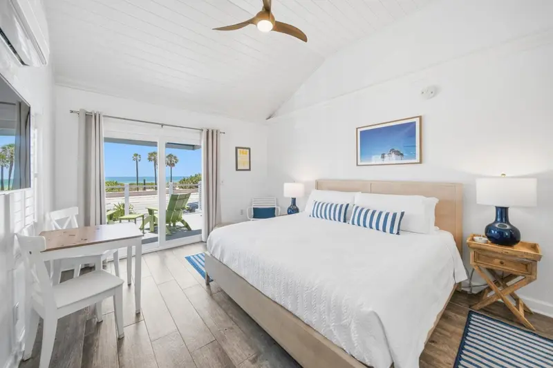 Chambre lumineuse avec un lit double et un coin repas près d'une baie vitrée.