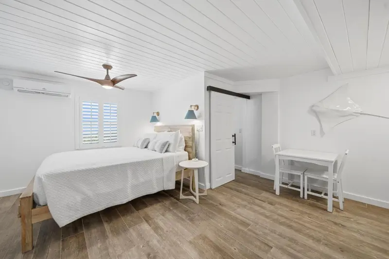 Chambre lumineuse avec un lit recouvert d'un drap blanc et une petite table.