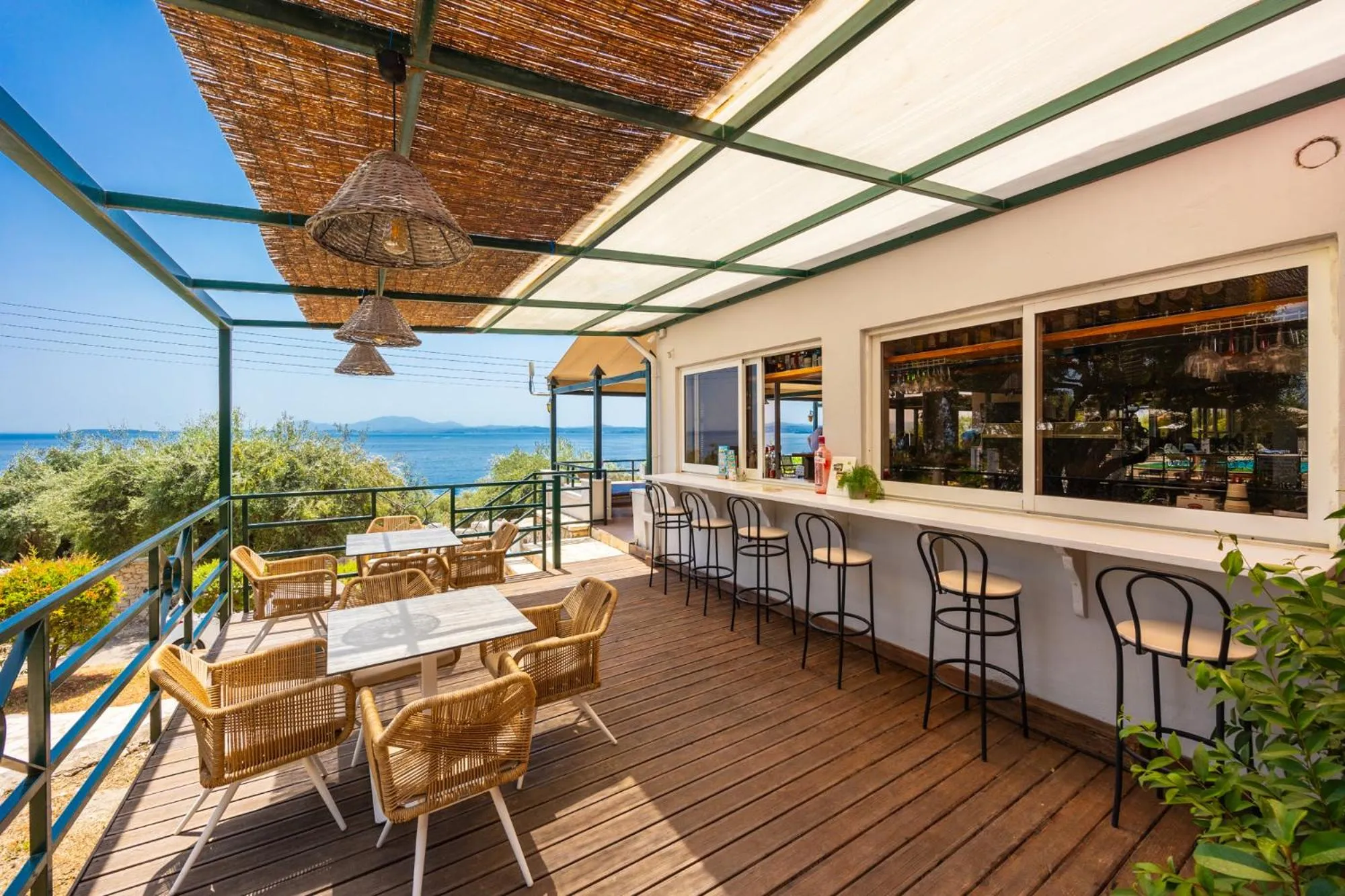 Terrasse ombragée avec tables et bar donnant sur la mer.