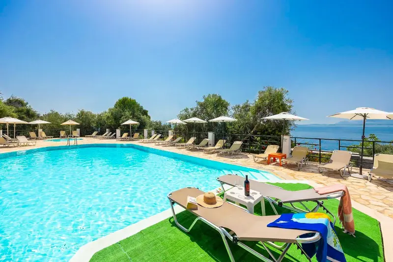 Transats et parasols bordent une piscine avec vue sur la mer.
