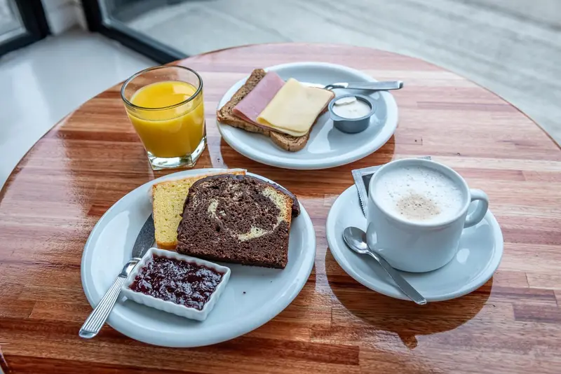 Une table ronde en bois présente un petit-déjeuner avec des viennoiseries, des tartines et des boissons.