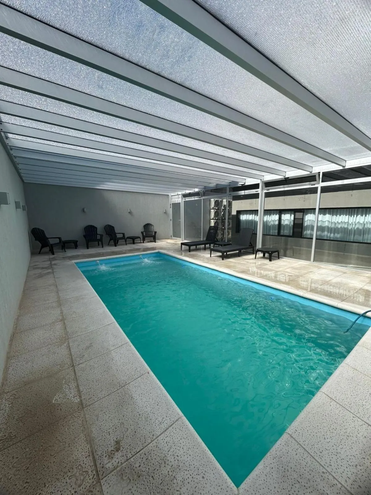 Une piscine rectangulaire turquoise est entourée de chaises longues sous une structure ombragée.
