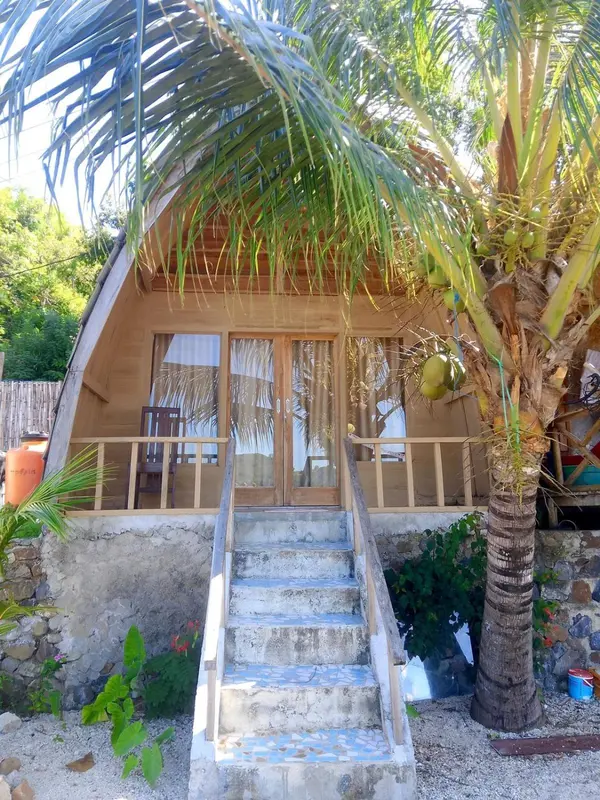 Petite maison en bois avec un escalier en pierre et une végétation tropicale.