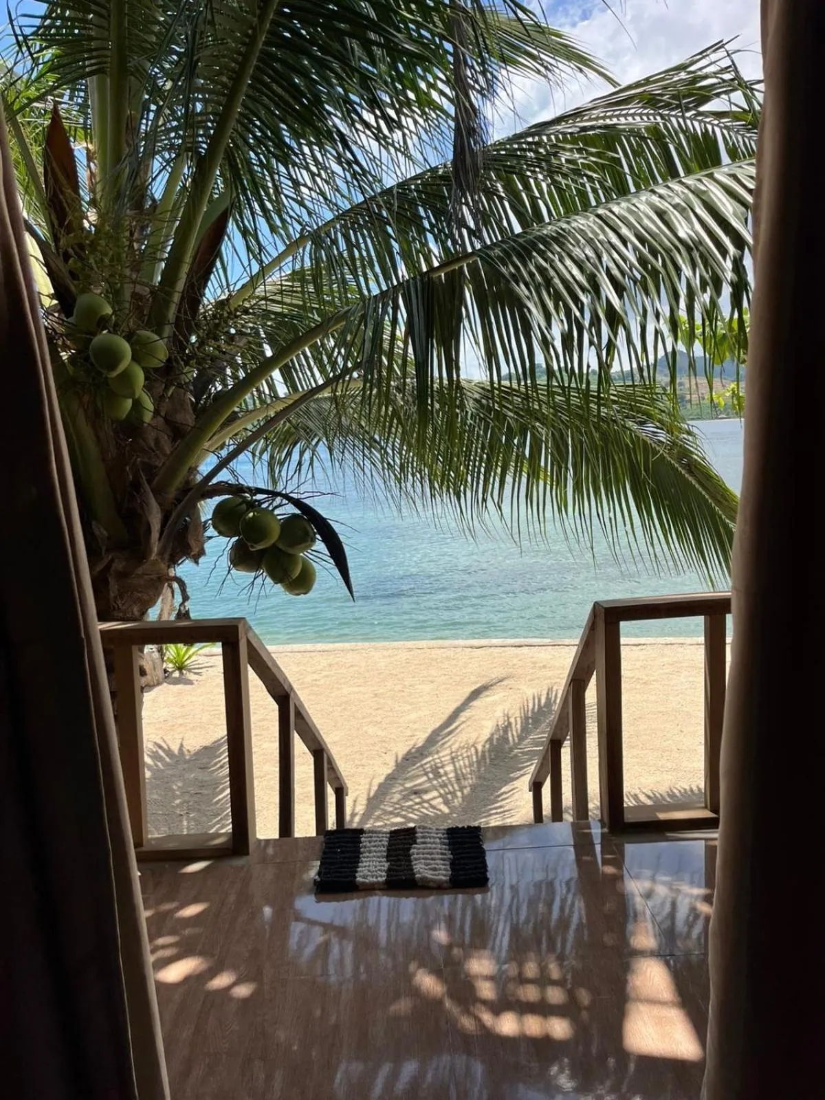 Une vue sur une plage de sable fin et la mer depuis une terrasse ombragée.