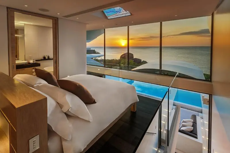 Une chambre avec un grand lit face à une baie vitrée donnant sur l'océan au coucher du soleil.