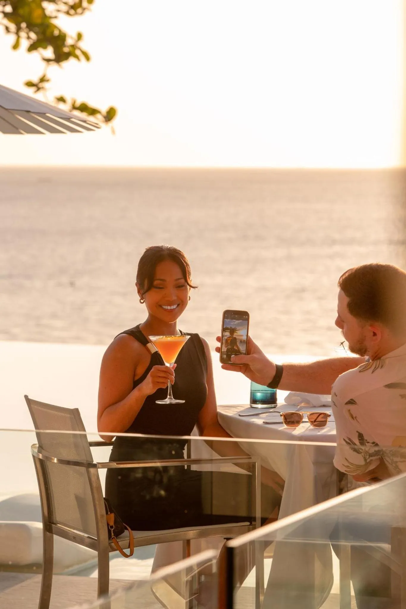 Un couple prend un verre sur une terrasse ensoleillée avec vue sur la mer.