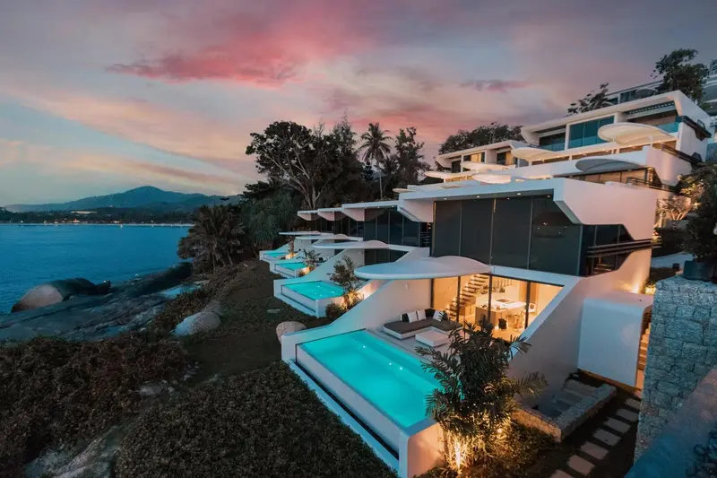 Architecture moderne blanche avec piscines privées surplombant la mer au coucher du soleil.