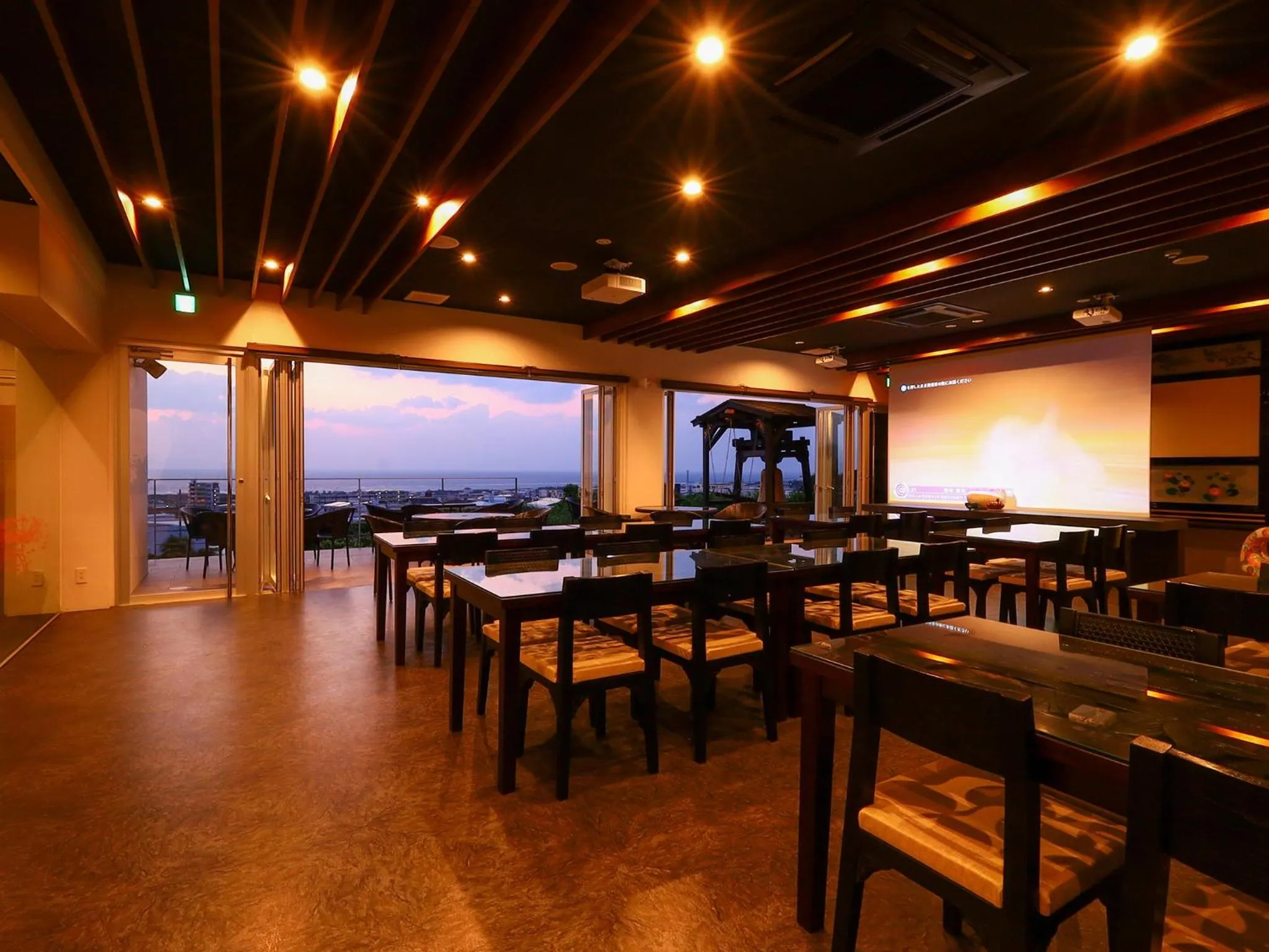 Une salle lumineuse avec des tables et des chaises offre une vue sur la mer au coucher du soleil.