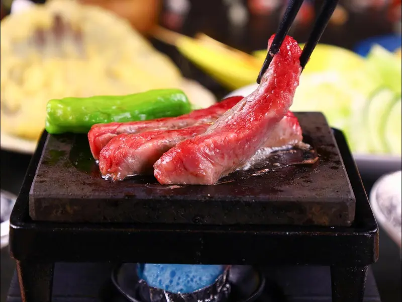 Des morceaux de viande et des légumes sont grillés sur une plaque chauffante.