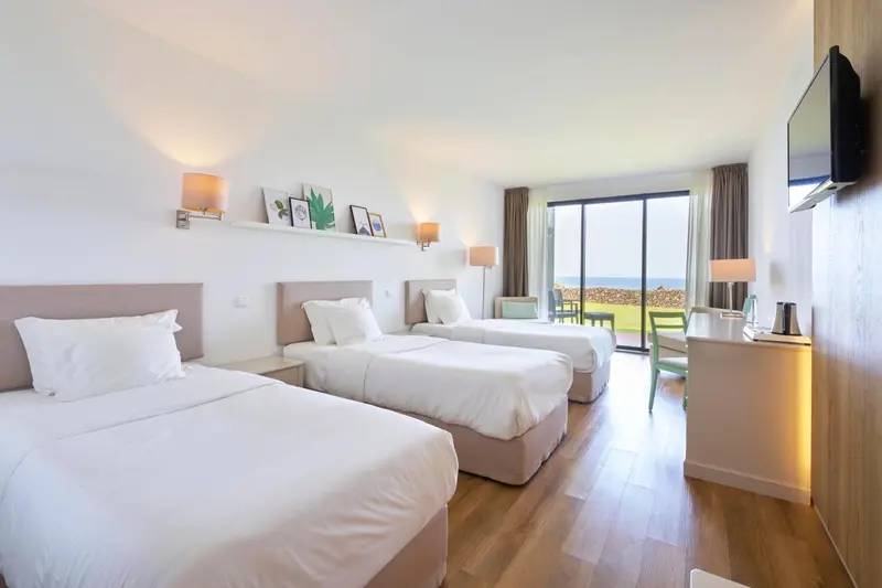 Chambre lumineuse avec deux lits simples et vue sur l'extérieur.