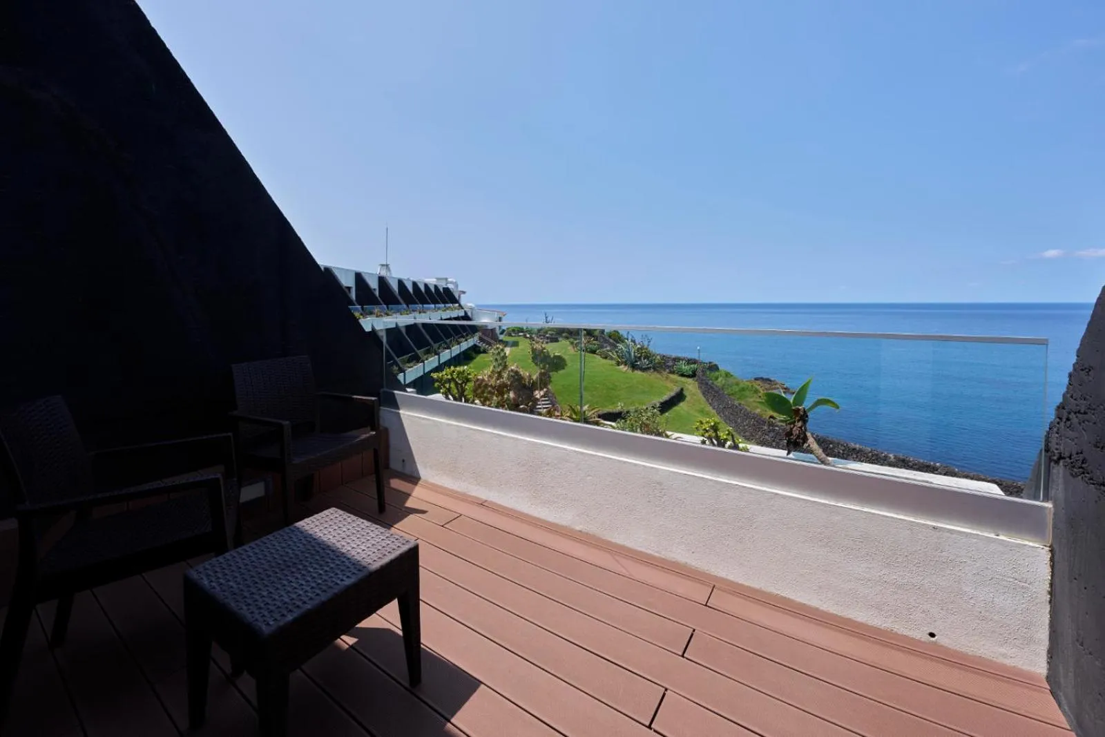 Terrasse avec mobilier en osier donnant sur la mer et la végétation.