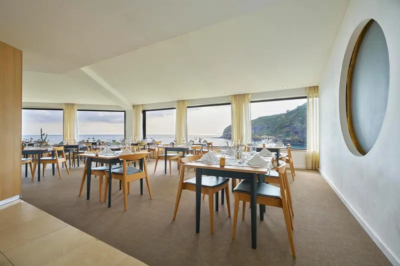 Une salle lumineuse avec des tables dressées face à une vue sur la mer.