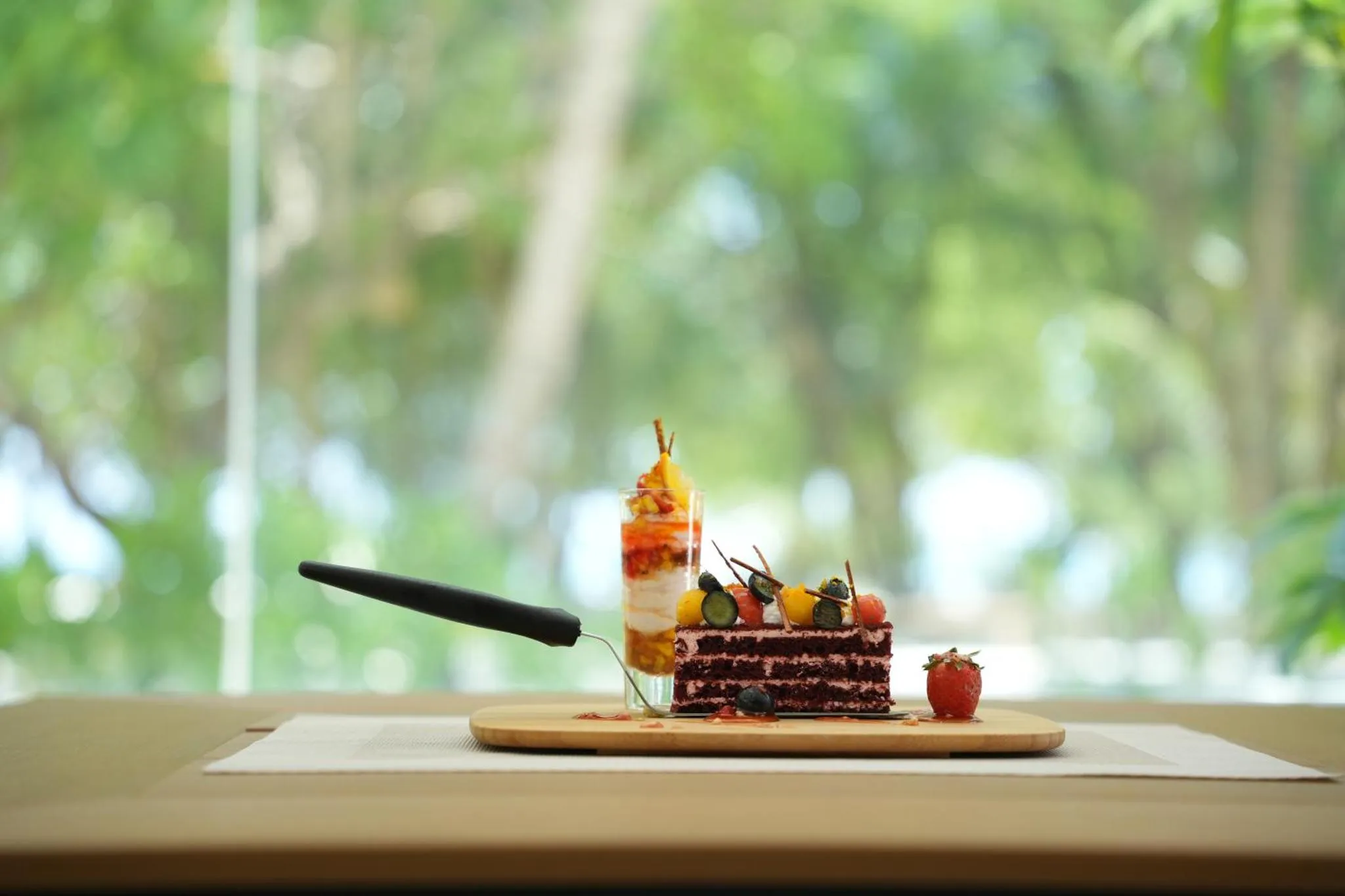 Une part de gâteau décorée de fruits frais est présentée sur une planche en bois.