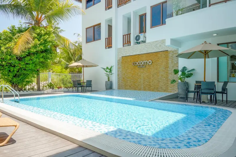 Piscine turquoise bordée d'une terrasse avec parasols et mobilier de jardin.