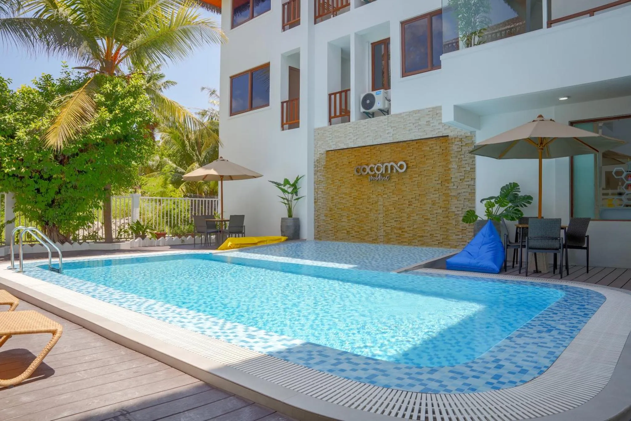 Une piscine turquoise bordée d'une terrasse en bois avec des transats et des parasols.