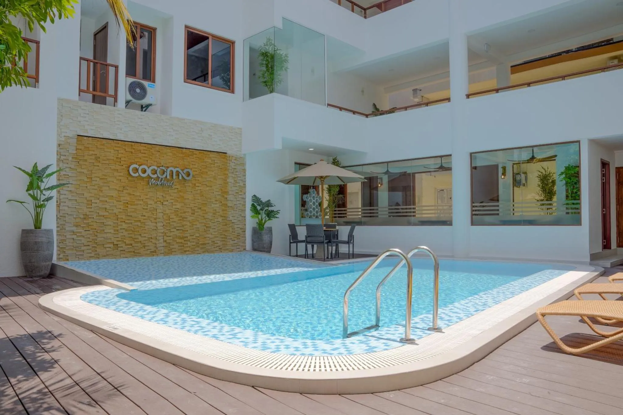 Une piscine rectangulaire turquoise est entourée d'une terrasse avec des transats et des plantes.