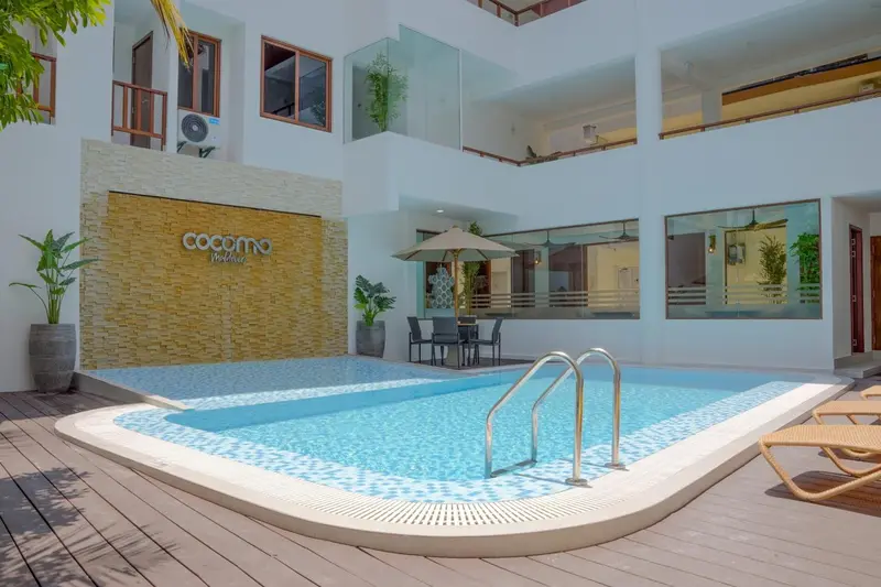 Une piscine rectangulaire turquoise est entourée d'une terrasse avec des transats et des plantes.