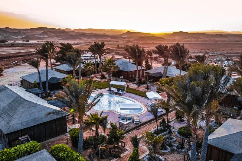Vue aérienne d'un complexe hôtelier avec piscine et végétation luxuriante au coucher du soleil.