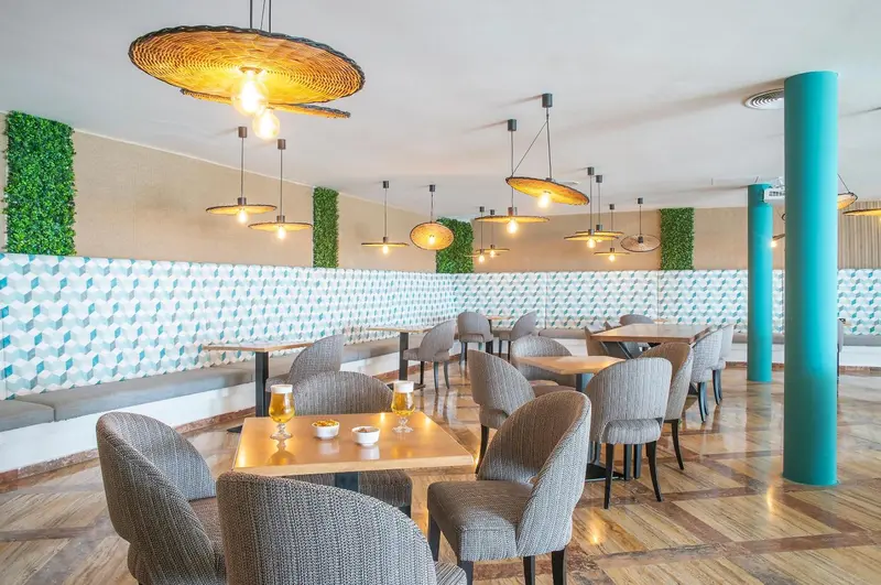 Une salle lumineuse avec des tables et des chaises, décorée de luminaires suspendus et d'un mur végétal.