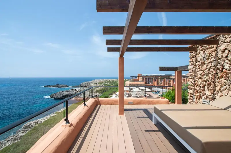 Terrasse en bois avec transats donnant sur la mer et le littoral rocheux.