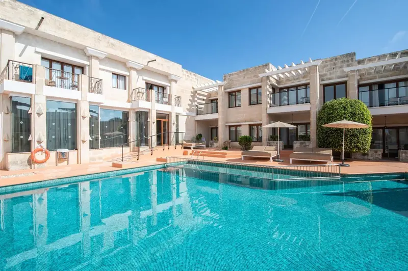 Piscine turquoise bordée de transats devant un bâtiment clair.