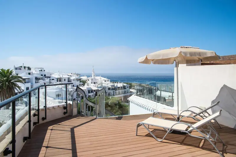 Terrasse en bois avec transats et vue sur la mer et un village.
