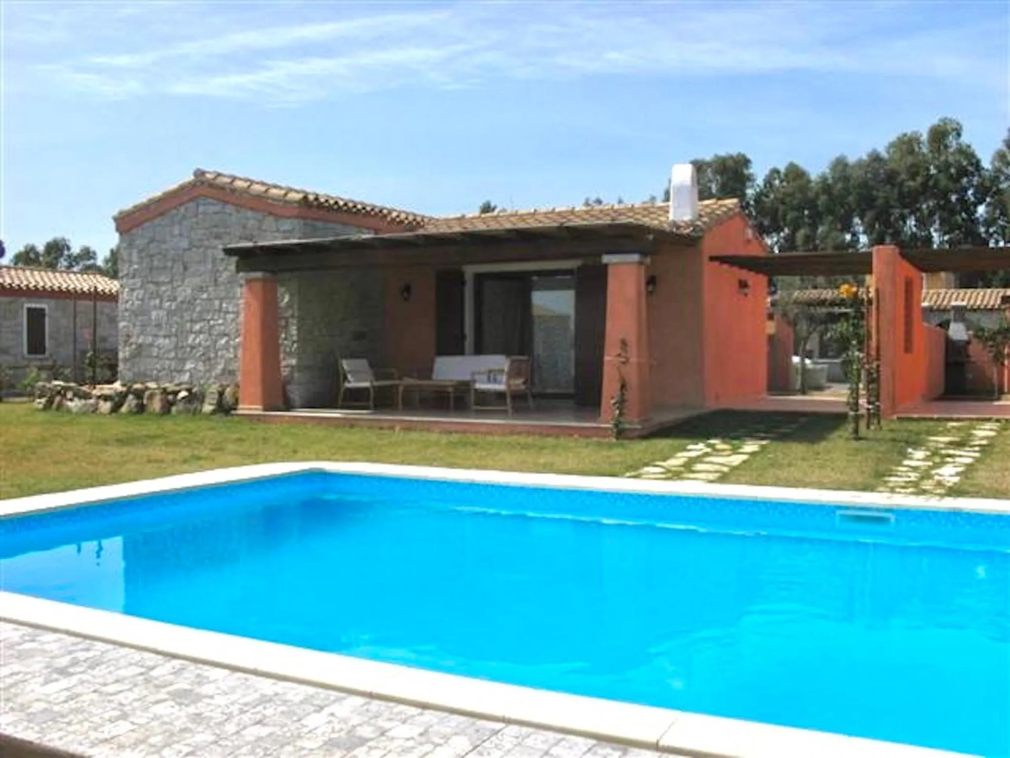 Maison basse aux murs clairs et à la terrasse ombragée, avec piscine au premier plan.